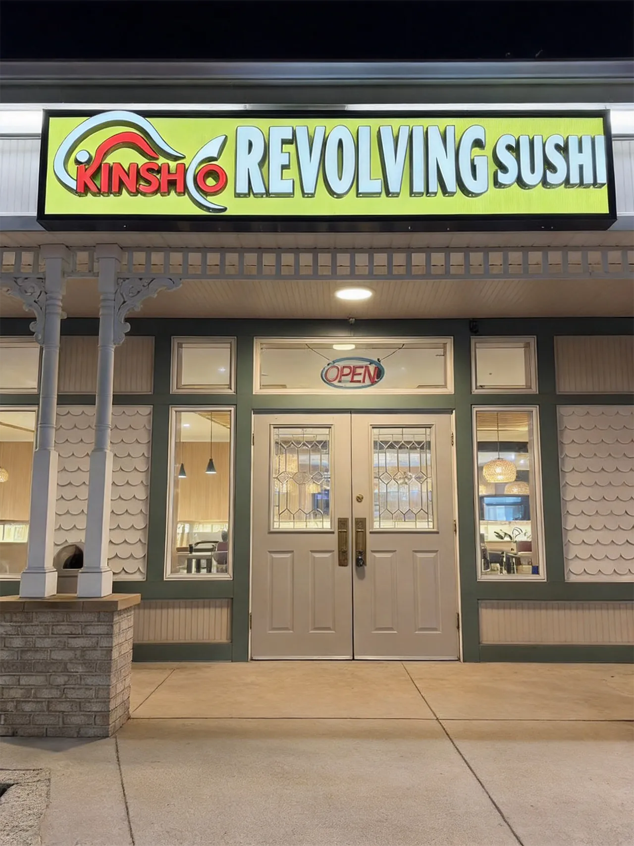 Exterior view of Kinsho Revolving Sushi restaurant with a bright yellow sign above white double doors.